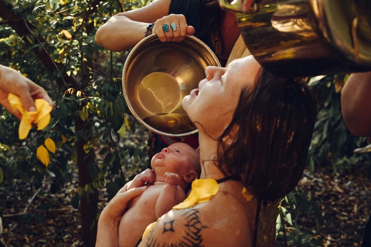 Newborn welcomed with a water and flower-petal blessing outdoors