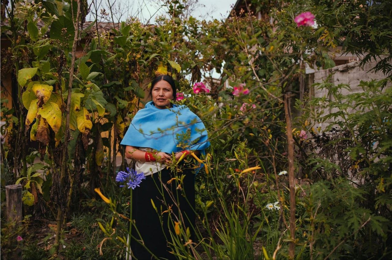 A Kichwa midwife stands in her garden among medicinal plants and flowers — Ecuadorian highlands