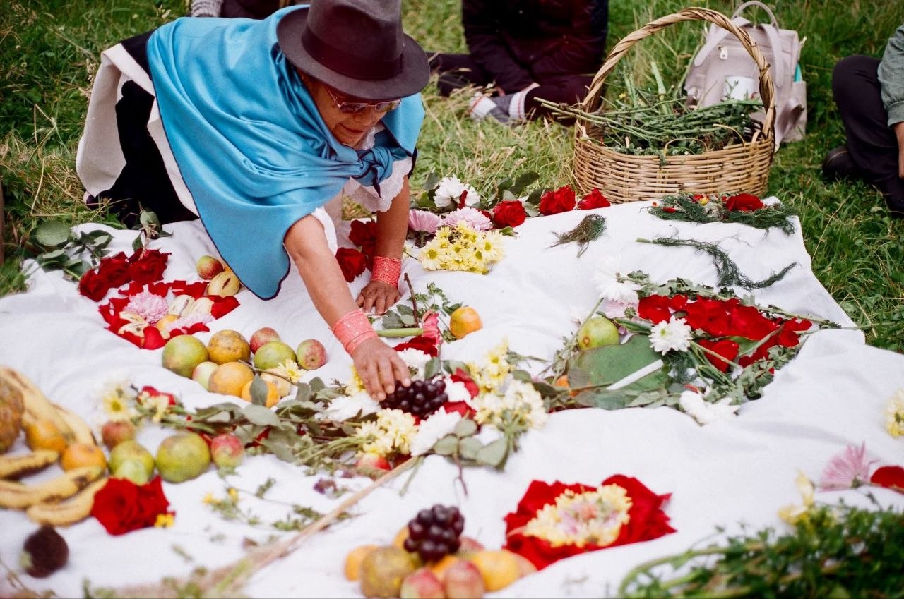 A Kichwa midwife arranges a ceremonial altar with fruits, flowers, and offerings in the Ecuadorian highlands